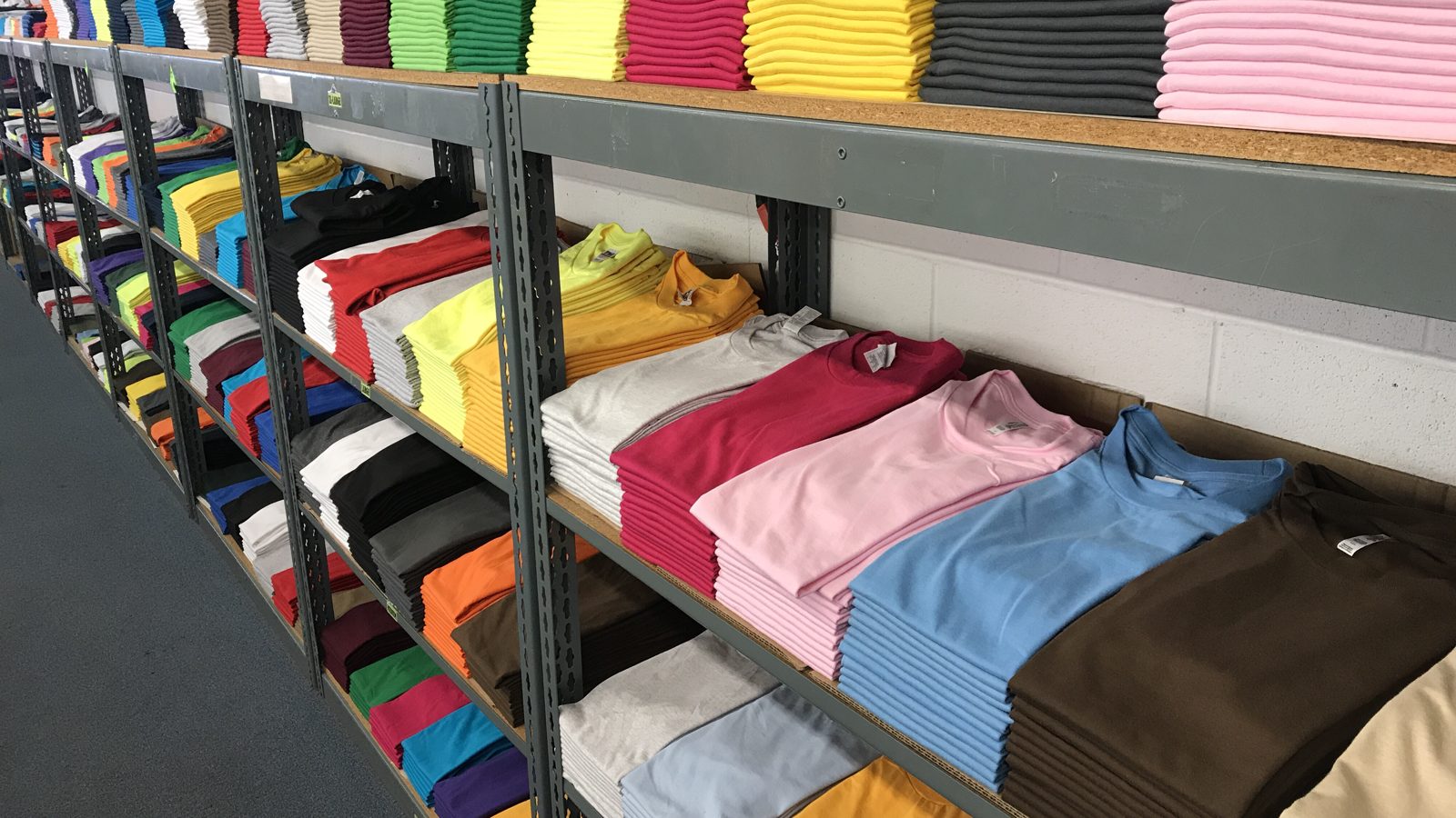 Long metal shelves of folded plain t-shirts sorted by color